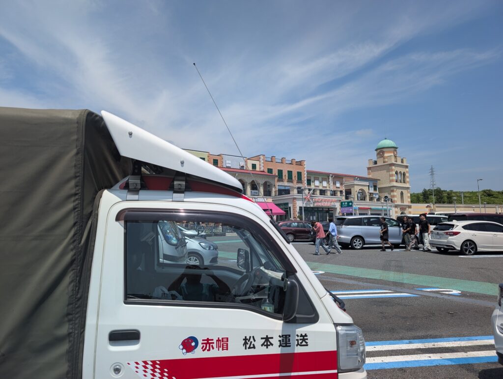 新東名高速の沼津サービスエリアに停車中の赤帽松本運送の車両。快晴の空と建物が印象的。