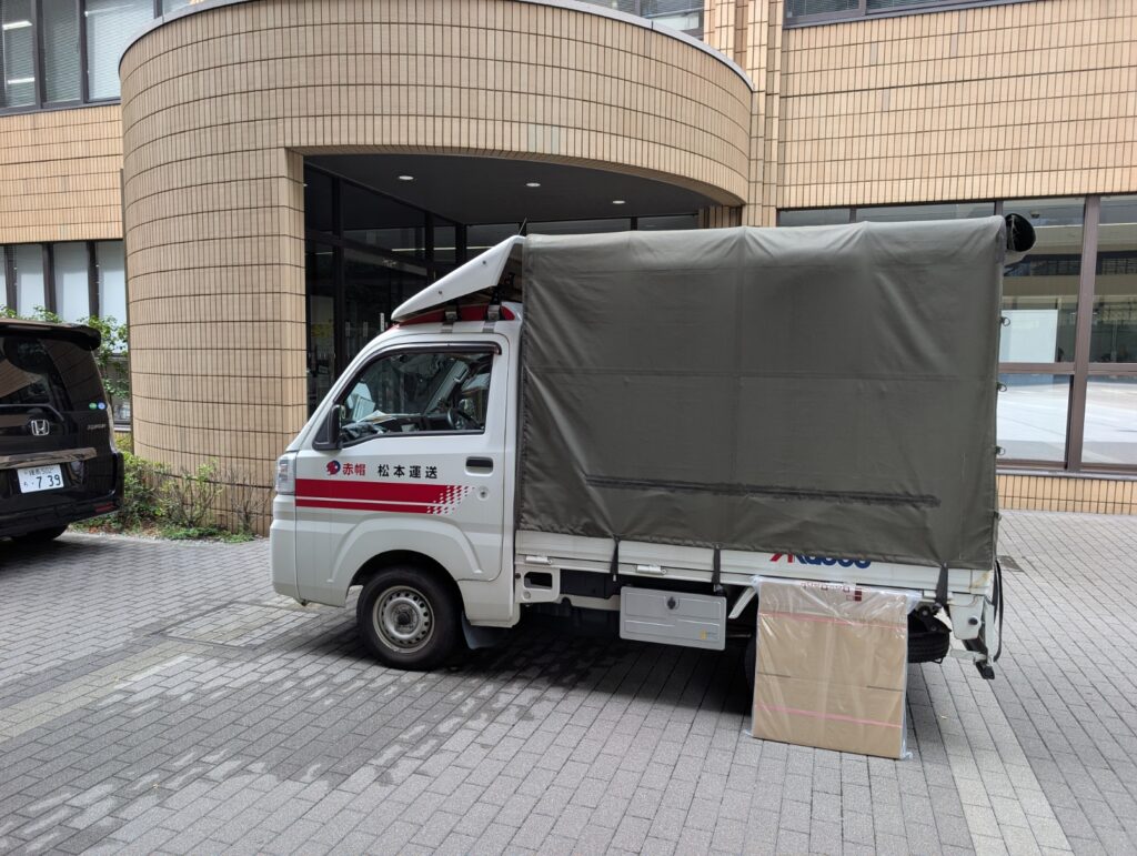 文京区の大学構内に駐車中の赤帽松本運送トラックと新品段ボール箱
