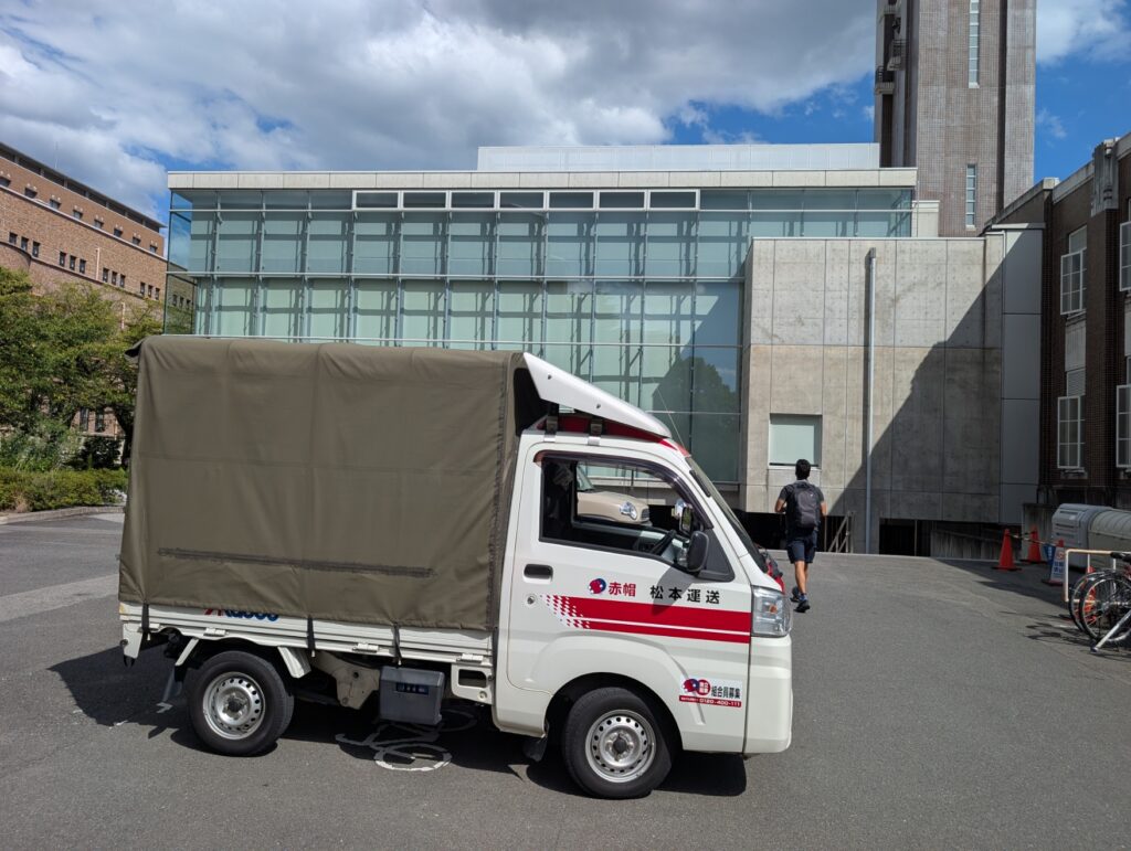 大学講堂の搬入出専用口に停車して待機する赤帽松本運送のトラック