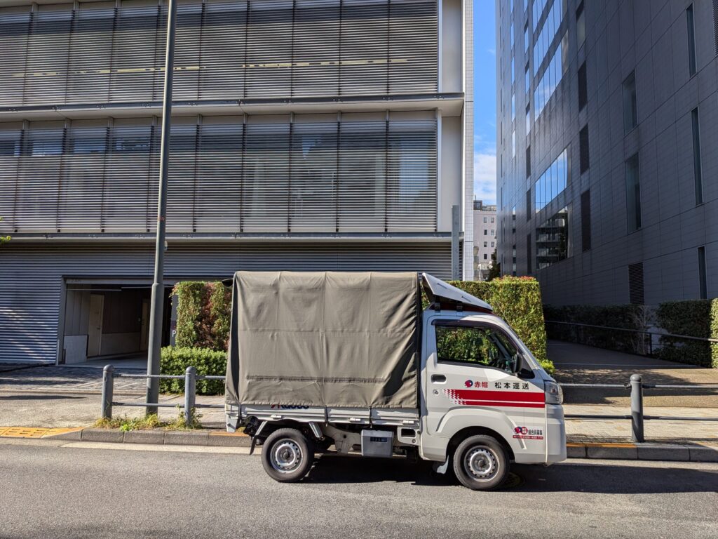 東京都千代田区のオフィス前に停車中の赤帽松本運送の幌付き軽トラック