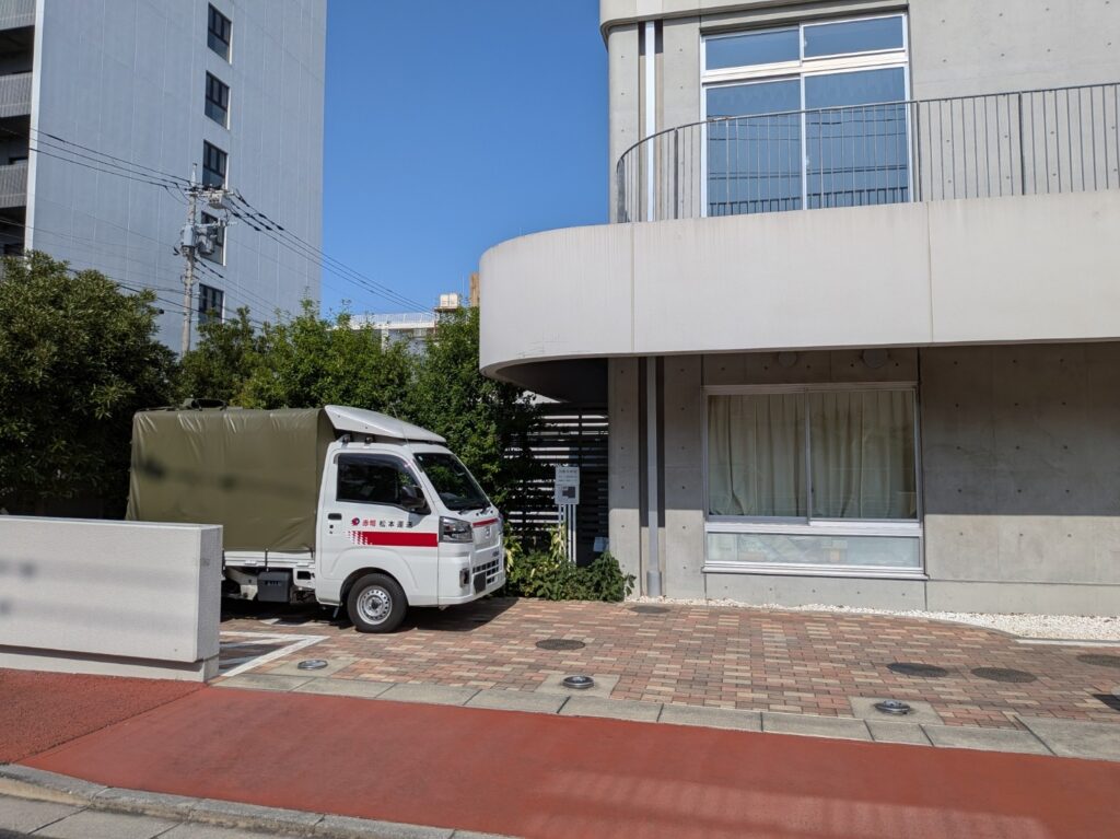 中学校で教材や資材を積み込むため校舎前に停車した赤帽松本運送トラック