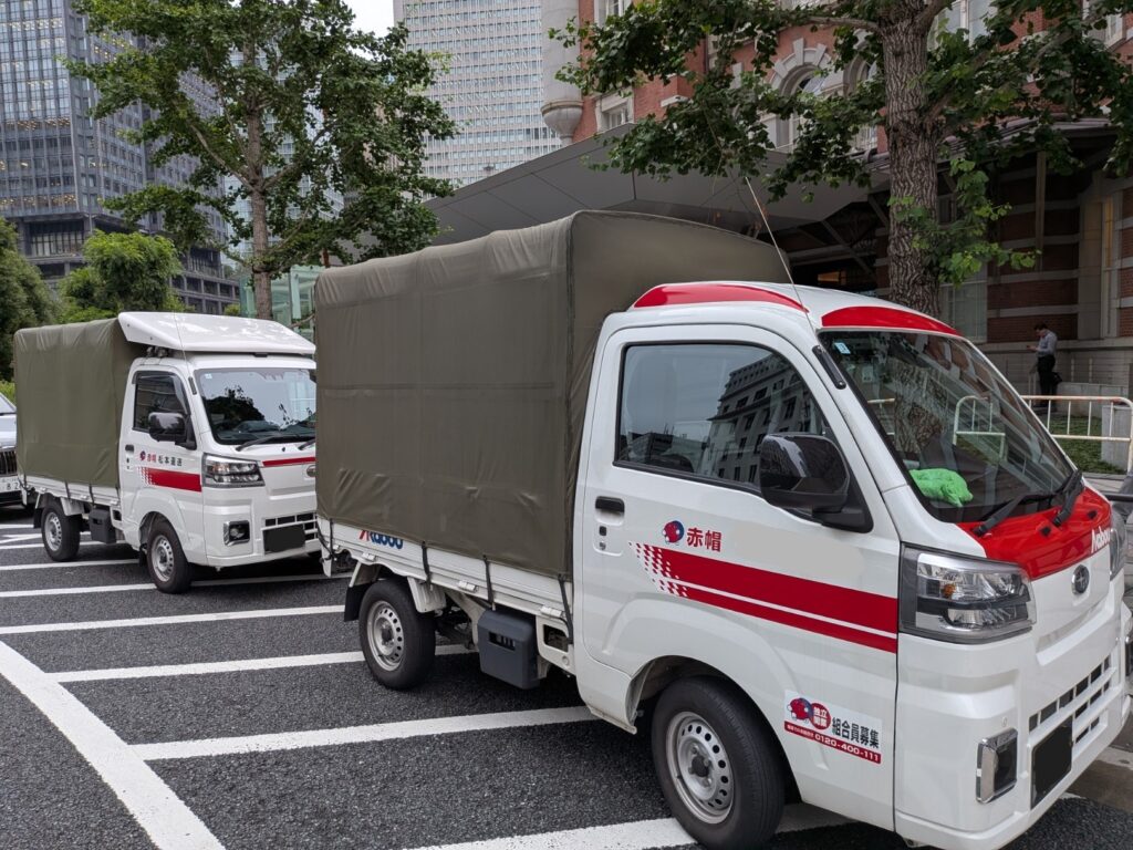 東京駅丸の内南口で修学旅行カバン配送を行う赤帽トラック2台