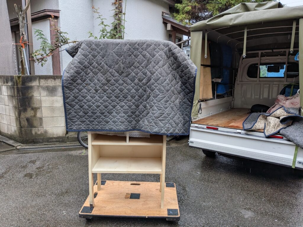雨の中、平台車で木製キャビネットを運搬