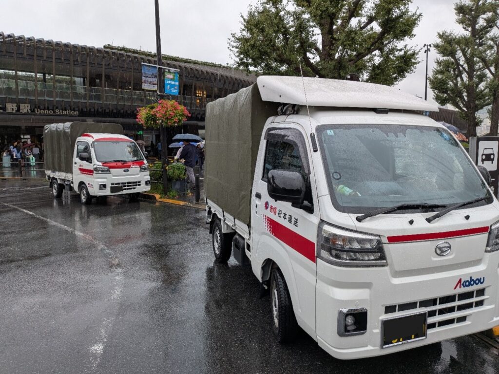 雨の上野駅公園口で修学旅行カバン配送に対応する赤帽2台