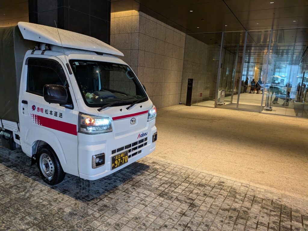 港区虎ノ門のオフィスビルの屋根付き車寄せで建築模型を荷下ろしする赤帽松本運送