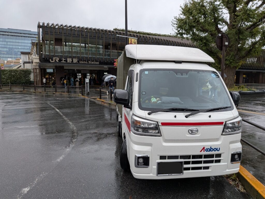 雨の上野駅公園口で修学旅行カバン配送に対応する赤帽車両